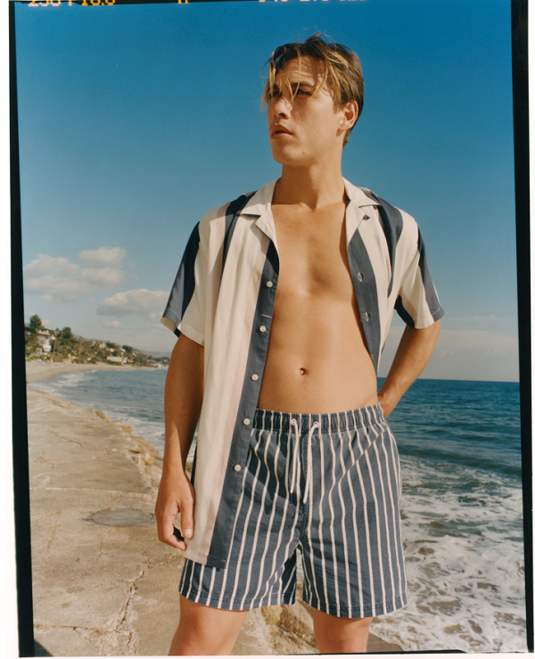 A model wearing striped swim shorts ad a striped shirt