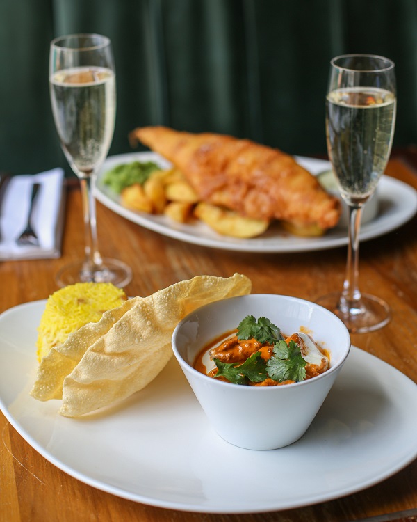 A curry and poppadom with fish and chips in the background.